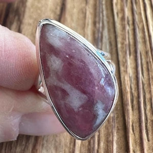 May include: A silver ring with a pink and white gemstone. The gemstone is a triangular shape with a smooth, polished surface.