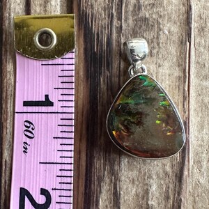 May include: A silver pendant with a teardrop-shaped iridescent opal stone. The stone has shades of green, brown, and gold. The pendant is approximately 1 inch in length.