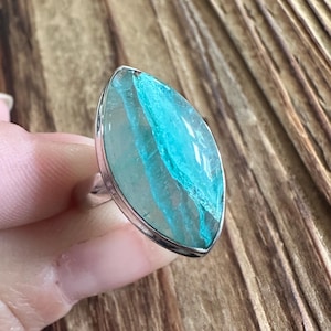 May include: A silver ring featuring a large, oval-shaped gemstone with a striking blue and turquoise pattern. The gemstone is set in a polished silver band, creating a bold and eye-catching piece of jewelry.