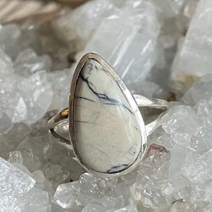 May include: A silver ring with a white and gray teardrop-shaped stone set in a silver bezel.