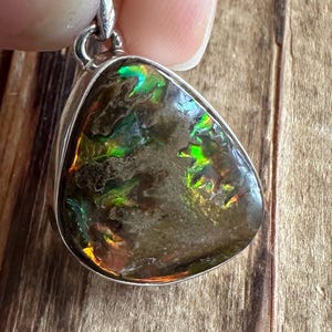 May include: A silver pendant featuring a teardrop-shaped iridescent opal with green, blue, and orange hues. The opal is set in a silver bezel and has a smooth, polished finish.