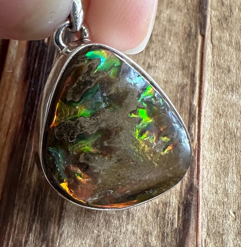 May include: A silver pendant featuring a teardrop-shaped iridescent opal with green, blue, and orange hues. The opal is set in a silver bezel and has a smooth, polished finish.