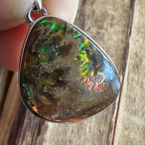 May include: A teardrop-shaped pendant with a silver bail and a brown, iridescent gemstone with green and red flashes.