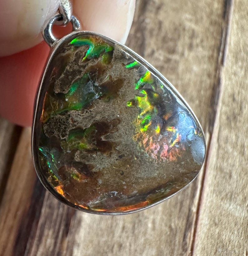May include: A teardrop-shaped pendant with a silver bail and a brown, iridescent gemstone with green and red flashes.