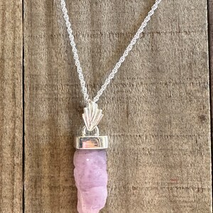 Puede incluir: Un collar de cadena de plata con un colgante que presenta un cristal crudo de color p&uacute;rpura claro. El cristal est&aacute; engastado en un bisel de plata y cuelga de una argolla de plata.