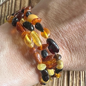 May include: A multi-strand bracelet featuring a variety of amber beads in shades of yellow, orange, brown, and black. The beads are of various shapes and sizes, strung together to create a unique accessory.