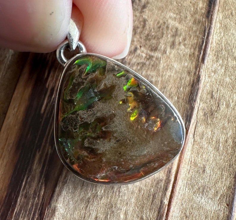 May include: A silver pendant featuring a teardrop-shaped iridescent opal with green and brown hues. The opal has a unique, swirling pattern.