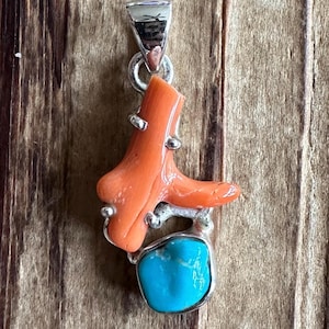 May include: A silver pendant featuring a bright orange coral branch and a turquoise stone. The pendant has a silver bail for attaching to a chain.