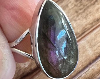 May include: A silver ring with a pear-shaped labradorite gemstone. The stone has a dark green base with iridescent purple and blue flashes.