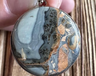 May include: A round silver pendant featuring a light blue, brown, and grey agate stone. The stone has a swirling pattern and a natural, organic appearance.