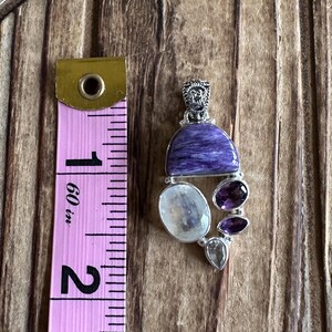 May include: A silver pendant with a purple and white gemstone design. The pendant is approximately 1 inch in length.