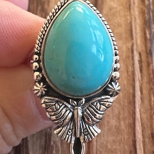 May include: A silver ring with a turquoise stone and a butterfly design.