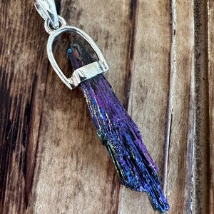 May include: A silver pendant featuring a long, iridescent purple and black crystal with a silver bail.