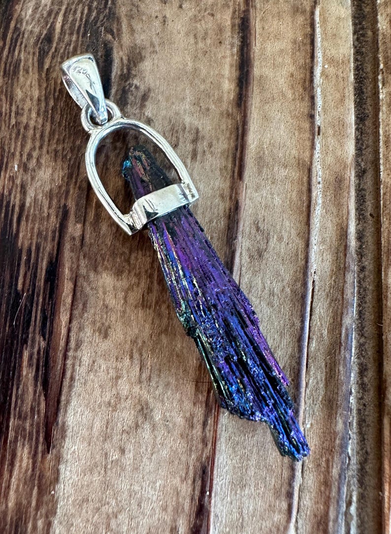 May include: A silver pendant featuring a long, iridescent purple and black crystal with a silver bail.