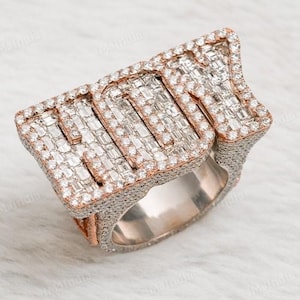 Könnte beinhalten: Ein Gold- und Silberring mit dem Wort "LOVE" in Baguette-Diamanten. Der Ring liegt auf einem weißen Fellhintergrund.