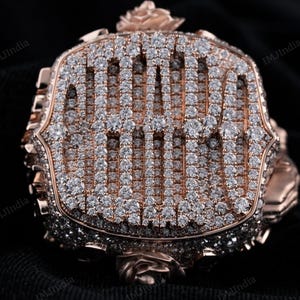 May include: A rose gold ring with a large square face set with diamonds. The ring is decorated with rose details on the sides.