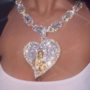 May include: A silver chain necklace with a large heart-shaped pendant encrusted with clear rhinestones. The pendant features a photo of a person inside.