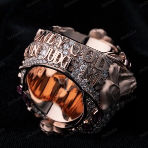 May include: A rose gold ring with a skull design and the words "Only God Can Judge Me" set in diamonds.
