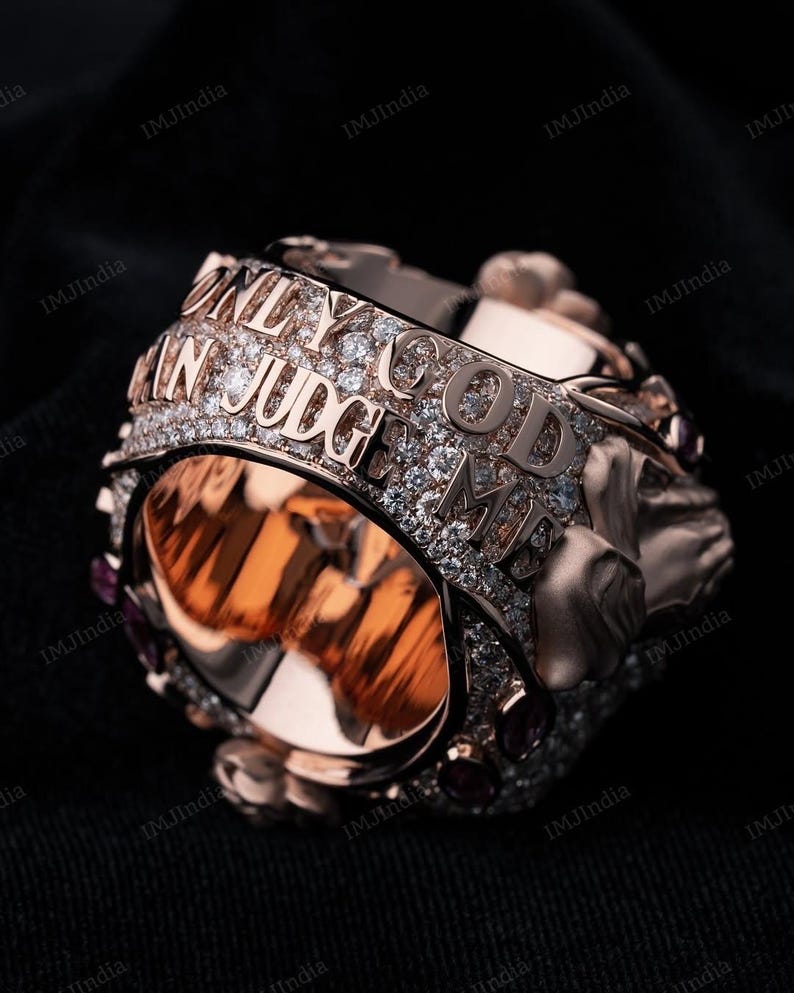 May include: A rose gold ring with a skull design and the words "Only God Can Judge Me" set in diamonds.