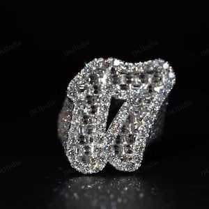 May include: A silver ring with a large, cubic zirconia letter 'W' set in the center. The letter is surrounded by smaller cubic zirconia stones.