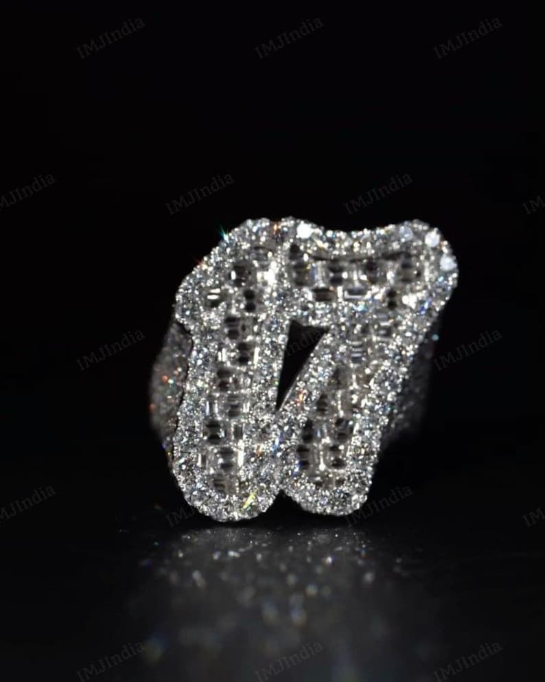 May include: A silver ring with a large, cubic zirconia letter 'W' set in the center. The letter is surrounded by smaller cubic zirconia stones.