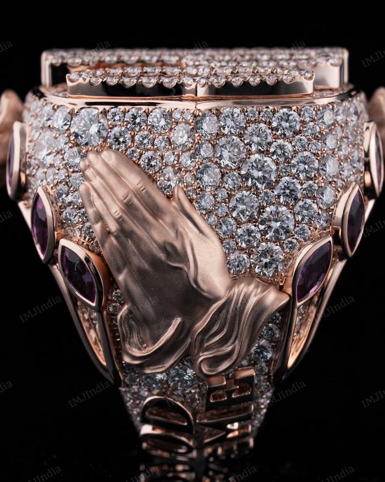 May include: A gold ring with a praying hands design, set with small diamonds and accented with purple gemstones.