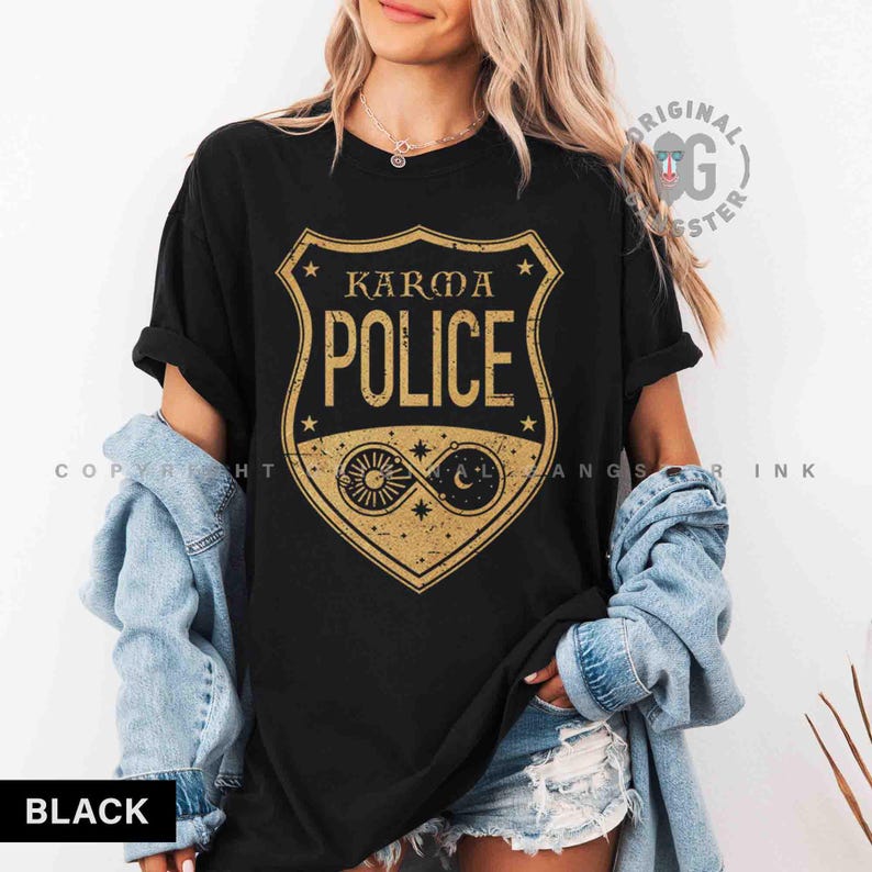 May include: Black t-shirt with a gold shield design that reads "Karma Police." The shield features stars, sun, moon, and infinity symbols. The shirt is a comfortable, casual style.