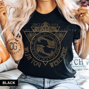 May include: Black t-shirt with a gold graphic design featuring a triangle with an eye inside, two fish swimming in a circle, and the text "Since 1975 We're Just Two Lost Souls Swimming In A Fish Bowl Wish You Were Here".