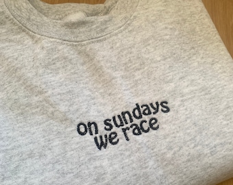 Op de afbeelding: Grijs sweatshirt met de tekst "on sundays we race" geborduurd in zwart.