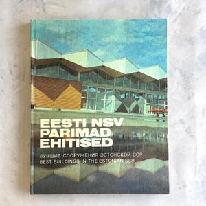 Può includere: Copertina di un libro vintage con il titolo "Eesti NSV Parimad Ehitised" e il testo "Best Buildings in the Estonian SSR". La copertina presenta un'illustrazione architettonica colorata di un edificio moderno con uno sfondo di cielo blu.