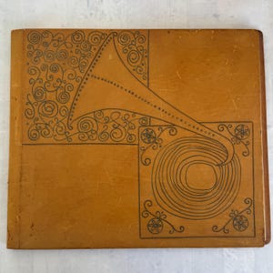 May include: A vintage-style, tan-colored book cover with a black line drawing of a gramophone. The design includes decorative swirls and floral elements. The cover has a slightly worn appearance.