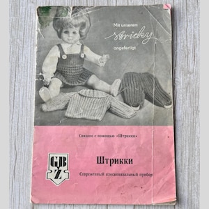 Puede incluir: Un folleto rosa y blanco con una foto de una muñeca con un atuendo tejido. El texto en el folleto dice "Mit unserem Stricky angefertigt" y "Связано с помощью «Штрикки»" y "Штрикки Современный плосковязальный прибор".