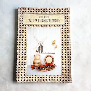 Könnte beinhalten: Ein Vintage-Buch mit dem Titel "Vits Punutised" von Uno Põlts. Das Cover zeigt einen gewebten Rand und eine zentrale Illustration einer Windmühle, einer Vase, eines Tellers und einer Schale mit Orangen. Das Buch hat einen hellen Hintergrund.