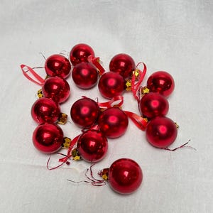 Puede incluir: Una colección de 14 adornos navideños rojos con detalles dorados. Los adornos son brillantes y tienen un ligero brillo metálico.