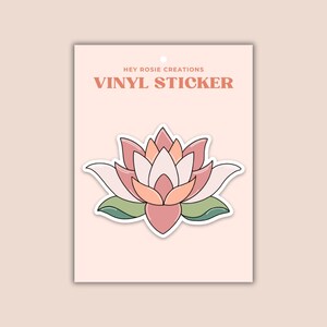 May include: A vinyl sticker featuring a stylized lotus flower with layered petals in shades of pink, peach, and white, accented by green leaves at the base. The sticker is displayed on a light pink backing card labeled HEY ROSIE CREATIONS VINYL STICKER.