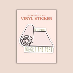 May include: A vinyl sticker on a display card featuring a light pink rolled yoga mat illustration. The text reads DO YOUR BEST above the mat and FORGET THE REST below it in olive green lettering. The brand name HEY ROSIE CREATIONS VINYL STICKER is printed at the top of the card.