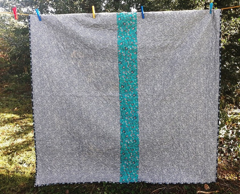 May include: A gray and white patterned quilt with a turquoise and white patterned border. The quilt is hanging on a clothesline.