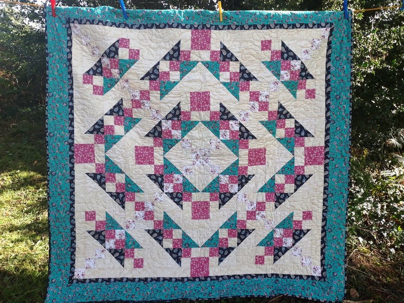 May include: A quilt with a patchwork design featuring a variety of fabrics in shades of pink, teal, white, and black. The quilt is made up of squares and triangles, creating a geometric pattern.