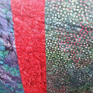 K&ouml;nnte beinhalten: Eine Steppdecke mit vier verschiedenen Stoffbahnen. Die Bahnen sind ein blaues und gr&uuml;nes Wirbelmuster, ein rotes Blumenmuster, ein gr&uuml;nes Punkte-Muster und ein blaues und gr&uuml;nes Wirbelmuster.