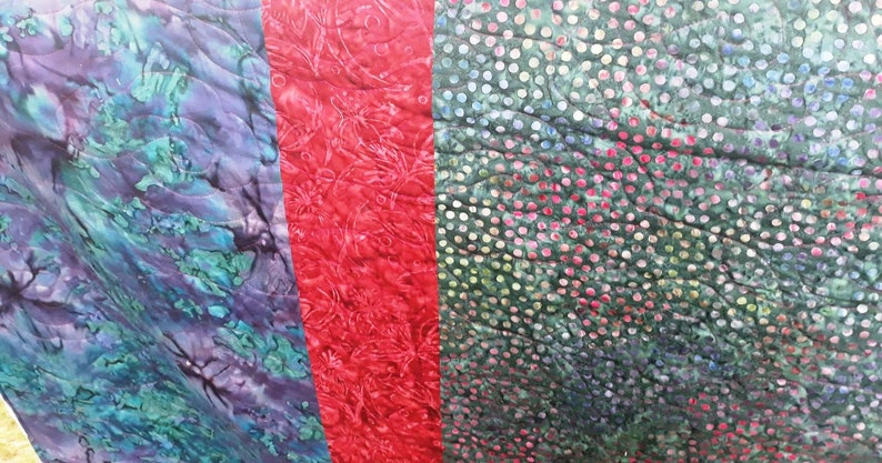 K&ouml;nnte beinhalten: Eine Steppdecke mit vier verschiedenen Stoffbahnen. Die Bahnen sind ein blaues und gr&uuml;nes Wirbelmuster, ein rotes Blumenmuster, ein gr&uuml;nes Punkte-Muster und ein blaues und gr&uuml;nes Wirbelmuster.