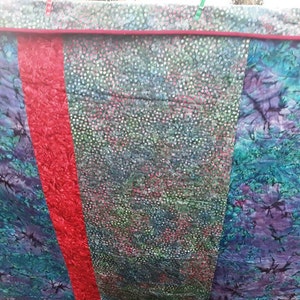 K&ouml;nnte beinhalten: Eine Steppdecke mit drei Paneelen. Die linken und rechten Paneele sind aus blauem und gr&uuml;nem Batikstoff mit einem dunklen Muster. Das mittlere Paneel ist aus gr&uuml;nem und wei&szlig;em Stoff mit einem kleinen wei&szlig;en Punktmuster. Die Paneele sind mit einem roten Stoffstreifen zusammengen&auml;ht.