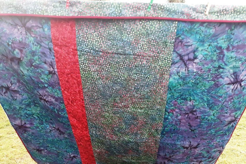 K&ouml;nnte beinhalten: Eine Steppdecke mit drei Paneelen. Die linken und rechten Paneele sind aus blauem und gr&uuml;nem Batikstoff mit einem dunklen Muster. Das mittlere Paneel ist aus gr&uuml;nem und wei&szlig;em Stoff mit einem kleinen wei&szlig;en Punktmuster. Die Paneele sind mit einem roten Stoffstreifen zusammengen&auml;ht.