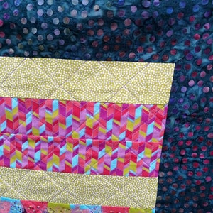 以下が含まれることがあります： 様々なカラフルな生地を使ったパッチワークのデザインのキルト。キルトは、水玉模様、ストライプ、幾何学模様など、さまざまなパターンで構成されています。キルトは、鮮やかでカラフルな芸術作品です。