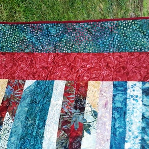 K&ouml;nnte beinhalten: Eine Steppdecke mit Patchwork-Muster in verschiedenen Blaut&ouml;nen, Rot und Wei&szlig;. Die Steppdecke ist aus Stoff mit Batik-Muster.