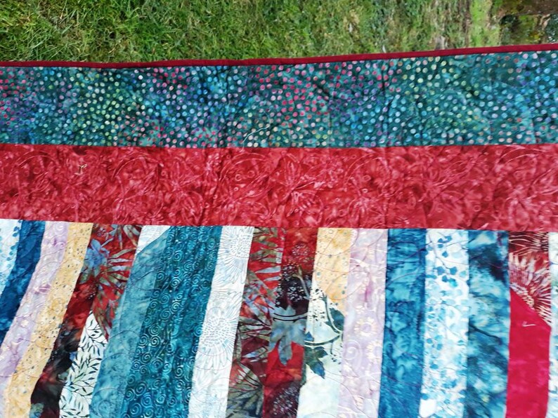 K&ouml;nnte beinhalten: Eine Steppdecke mit Patchwork-Muster in verschiedenen Blaut&ouml;nen, Rot und Wei&szlig;. Die Steppdecke ist aus Stoff mit Batik-Muster.