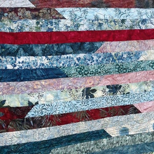 K&ouml;nnte beinhalten: Eine Decke aus verschiedenen blauen, gr&uuml;nen und roten Stoffen mit Blumenmustern. Die Decke besteht aus Stoffstreifen, die diagonal zusammengen&auml;ht sind.