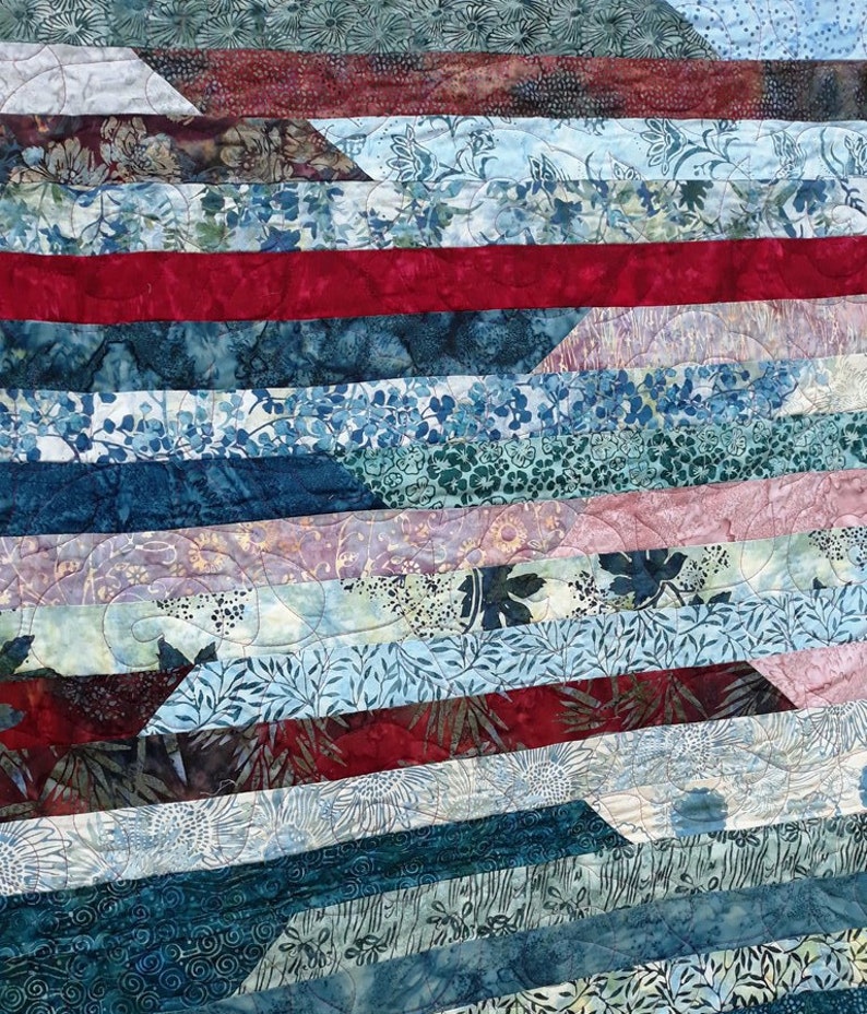 K&ouml;nnte beinhalten: Eine Decke aus verschiedenen blauen, gr&uuml;nen und roten Stoffen mit Blumenmustern. Die Decke besteht aus Stoffstreifen, die diagonal zusammengen&auml;ht sind.