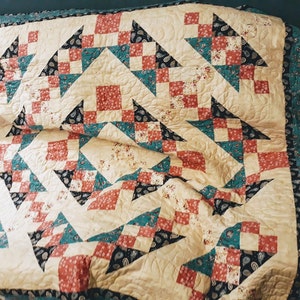May include: A quilt with a patchwork design featuring a variety of colors, including red, teal, black, and cream. The quilt is made up of squares and triangles, and it has a quilted texture.