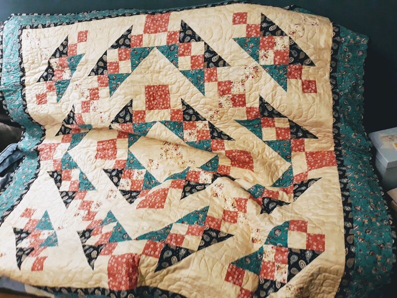 May include: A quilt with a patchwork design featuring a variety of colors, including red, teal, black, and cream. The quilt is made up of squares and triangles, and it has a quilted texture.