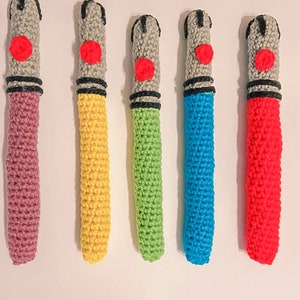 K&ouml;nnte beinhalten: F&uuml;nf handgefertigte H&auml;kel-Lichtschwerter in verschiedenen Farben. Jedes hat einen grauen Griff mit einem roten Knopf, ein schwarzes Band und eine farbige Klinge. Zu den Farben geh&ouml;ren Rosa, Gelb, Gr&uuml;n, Blau und Rot. Die Lichtschwerter sind vertikal angeordnet.